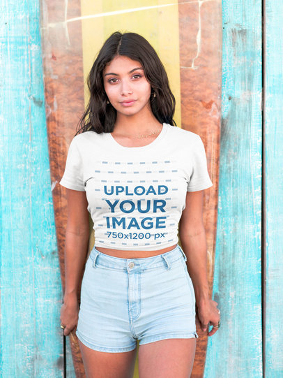Hispanic Woman Wearing a Tshirt Mockup Standing Against a Surfboard