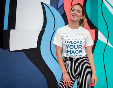 Tee Mockup of a Smiling Woman in Front of a Wall with Colorful Illustrations