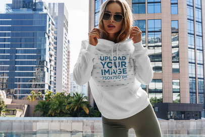 Hoodie Mockup Featuring a Woman Posing and Some Buildings in the Background 