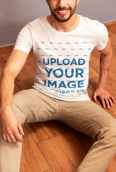 Bella Canvas T-Shirt Mockup Featuring a Smiling Cropped-Face Man Sitting on a Wooden Floor