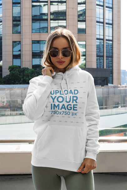 Mockup of a Woman with a Pullover Hoodie Posing by a Tall Building 