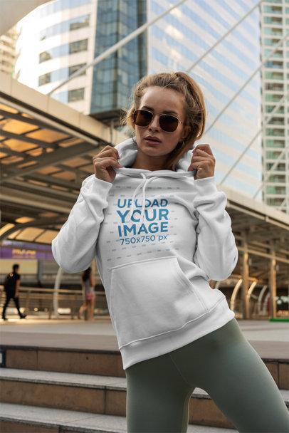 Mockup of a Trendy Woman Posing with a Hoodie Next to a Bridge